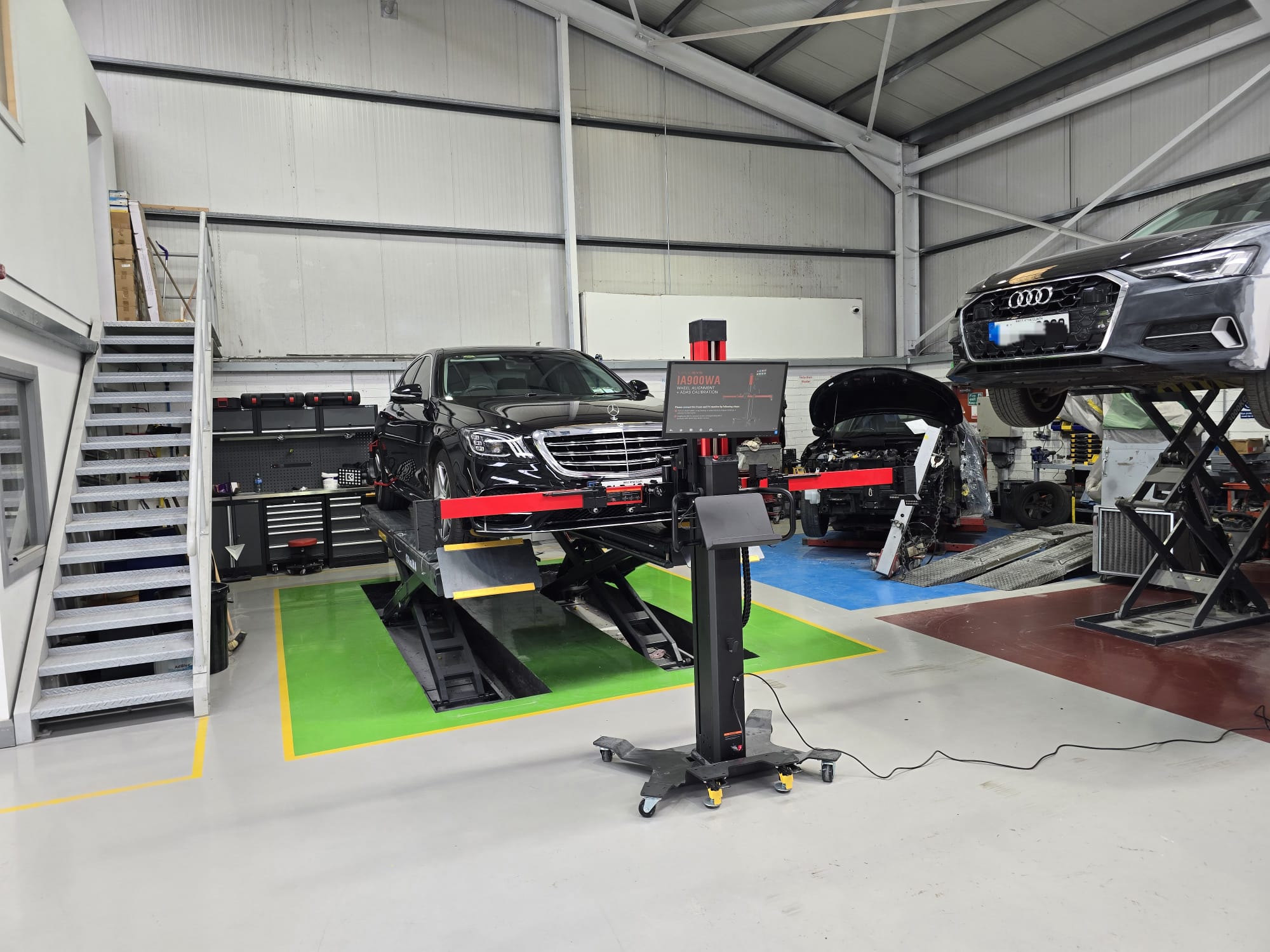 Black Mercedes in workshop undergoing wheel alignment - wide view.