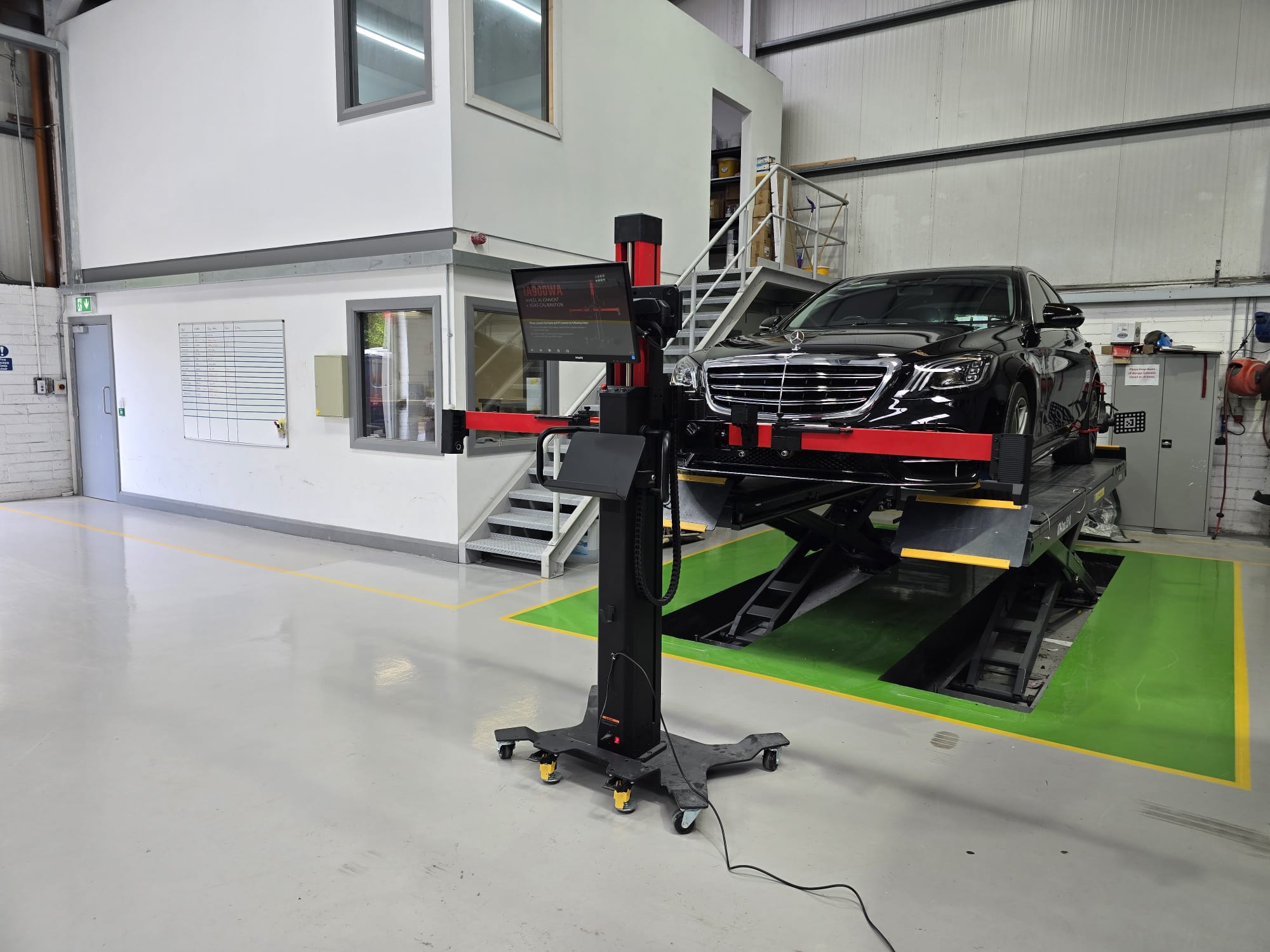 Black Mercedes in workshop undergoing wheel alignment.